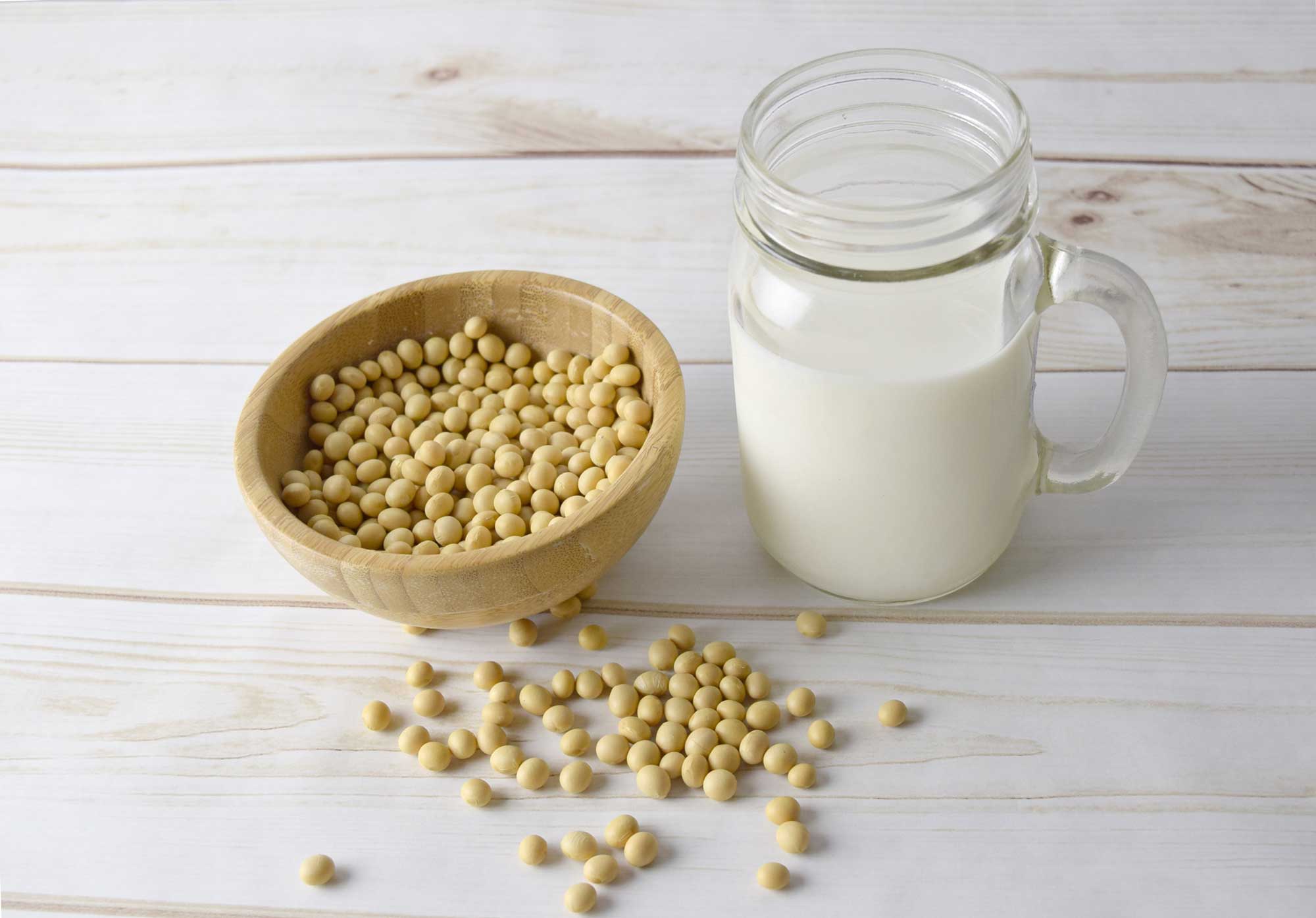 A bowl of soybeans next to a glass of milk.