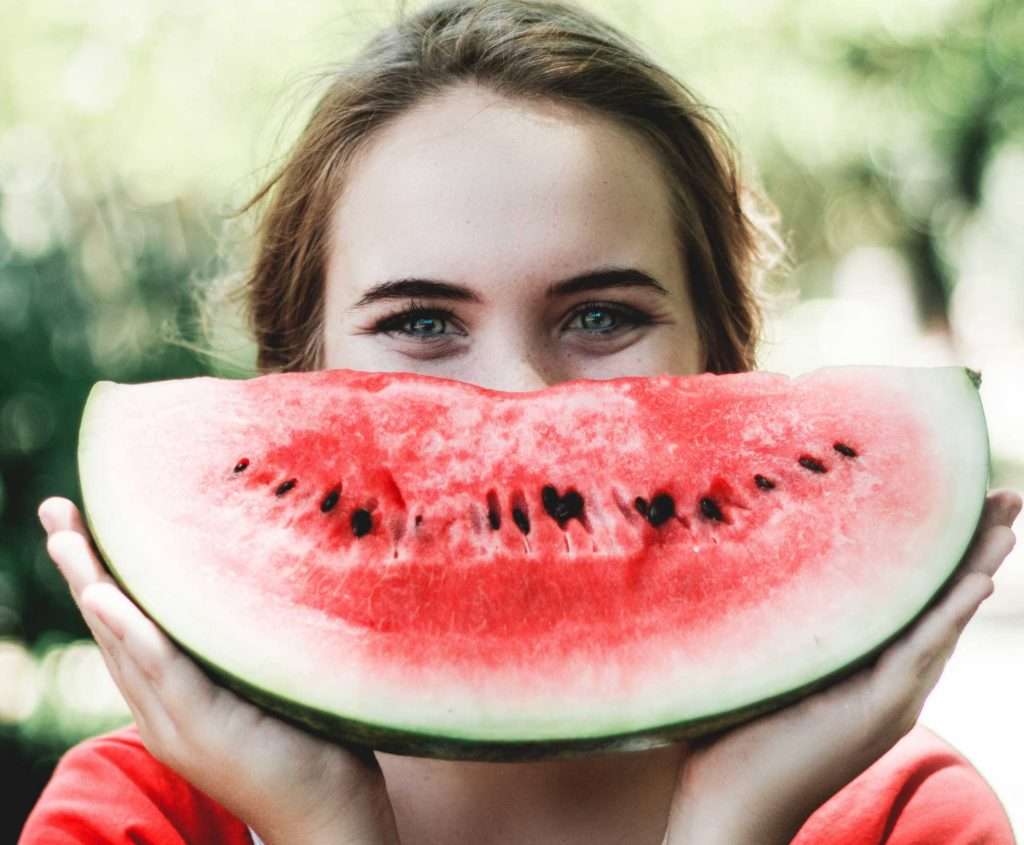 A woman holding up a watermelon to her face.